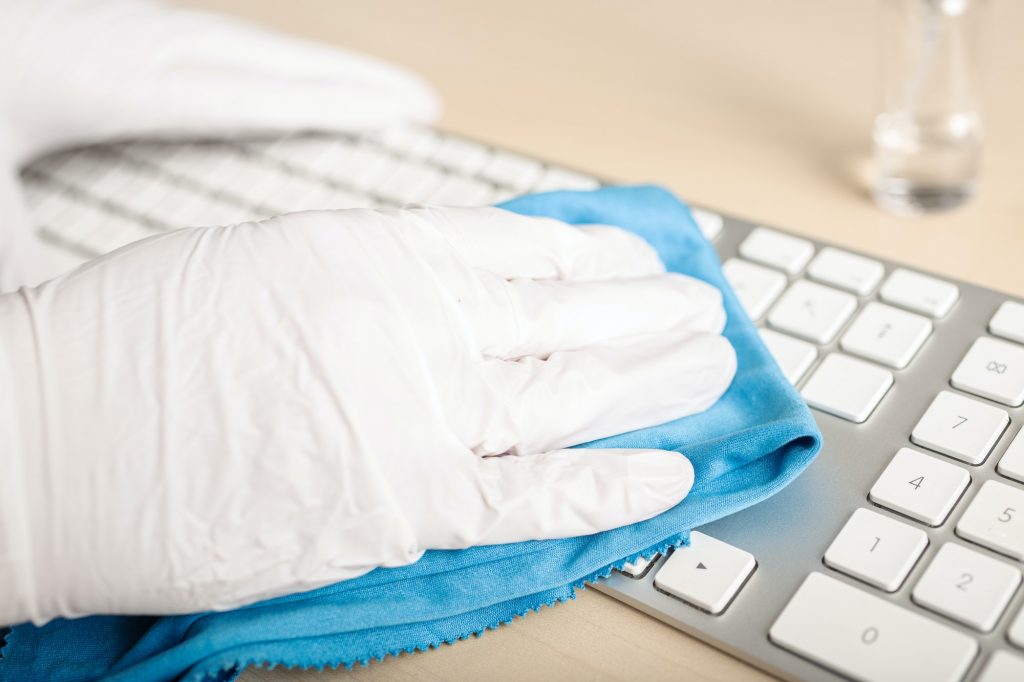Hand with protective glove cleaning a keyboard with disinfectant